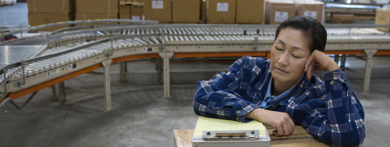 Asian woman half-asleep, leaning on shipping box at work