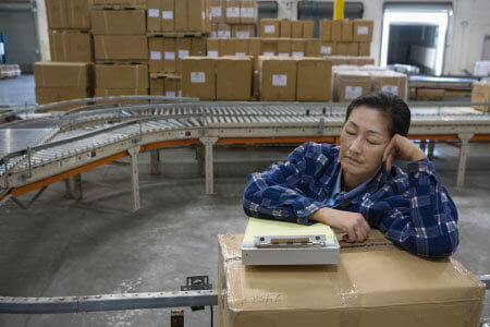 Asian woman half-asleep, leaning on shipping box at work